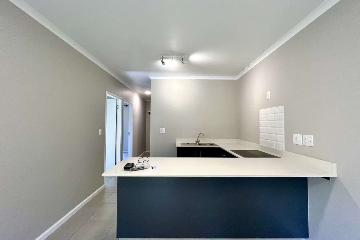 A clean, modern kitchen featuring a breakfast bar, built-in hob, sink, and subway tile backsplash with neutral wall finishes.