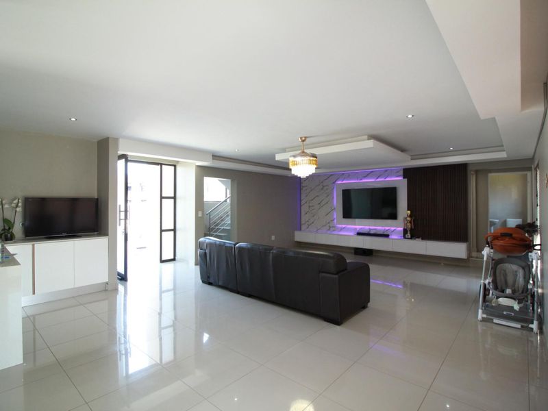 Spacious modern living room featuring high-gloss porcelain tiles, a custom built-in media wall with integrated LED lighting, and elegant ceiling detailing.