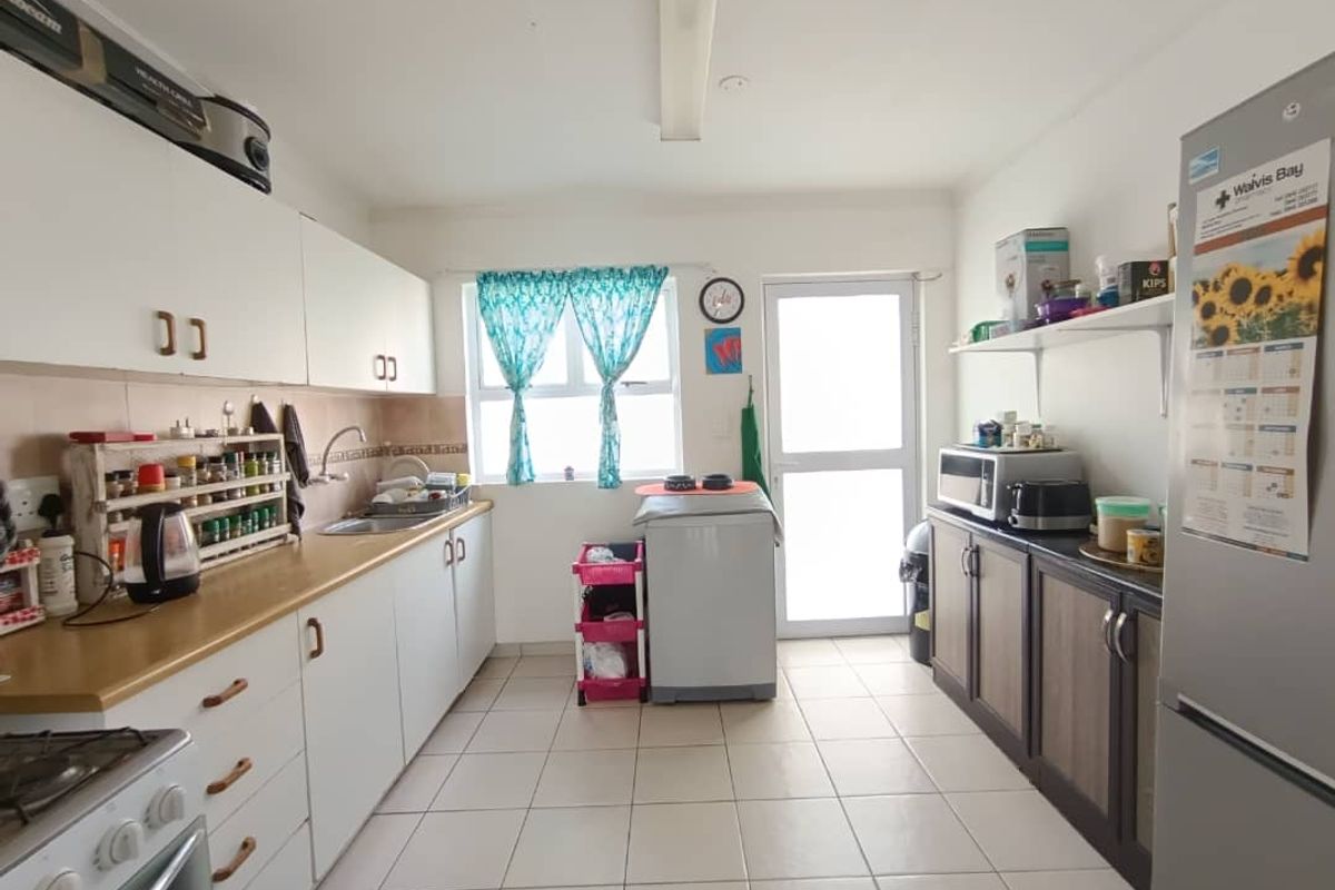 Functional kitchen featuring white and wood-tone cabinetry, laminate countertops, tiled flooring, and direct access to the exterior via a glass-paneled door.