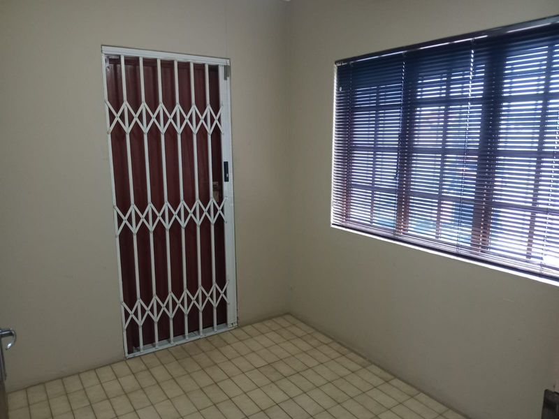 An empty bedroom featuring tiled flooring, a security gate, and window blinds, offering a blank canvas for potential renovation or restyling.