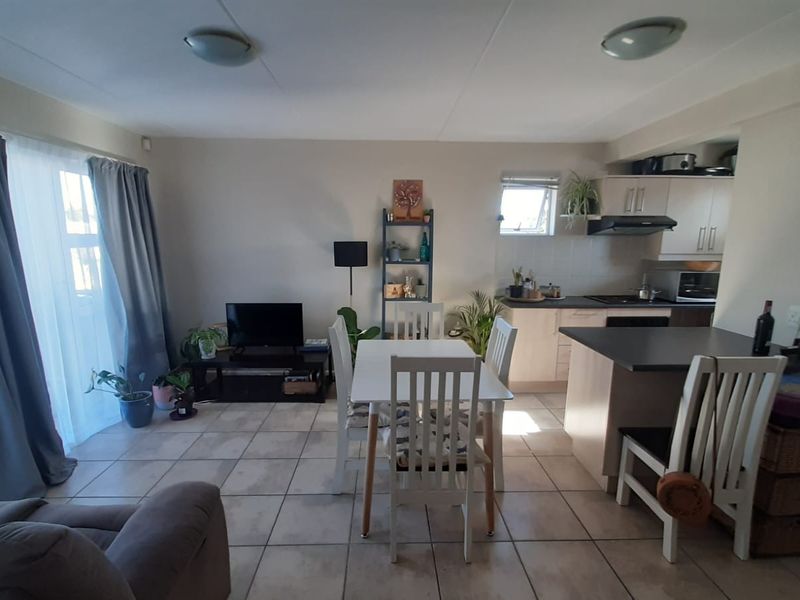 Open-plan living and dining area featuring tiled floors, a functional kitchen with island, and direct access to a balcony through sliding glass doors.
