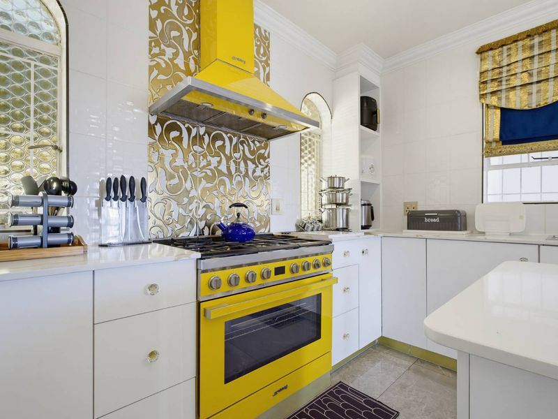 A bright kitchen featuring white cabinetry, stone countertops, and a bold yellow Smeg gas stove with a matching extractor fan and decorative backsplash.