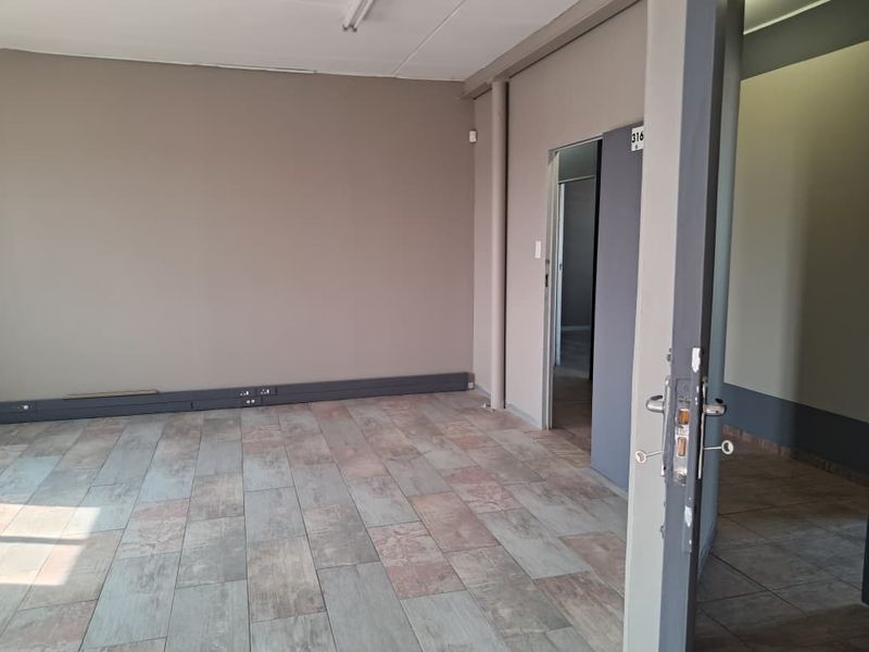 An empty office space featuring tiled flooring, surface-mounted electrical trunking, and neutral wall finishes, suitable for a professional workspace setup.