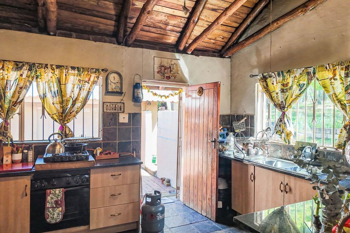 Rustic kitchen featuring exposed timber ceiling beams, dark stone countertops, built-in cabinetry, and a gas stove, with direct access to an outdoor area.