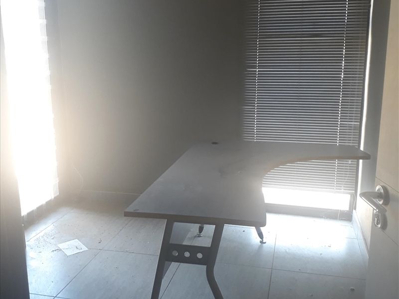 A functional office space featuring tiled flooring, venetian blinds, and natural light access through a glass sliding door.