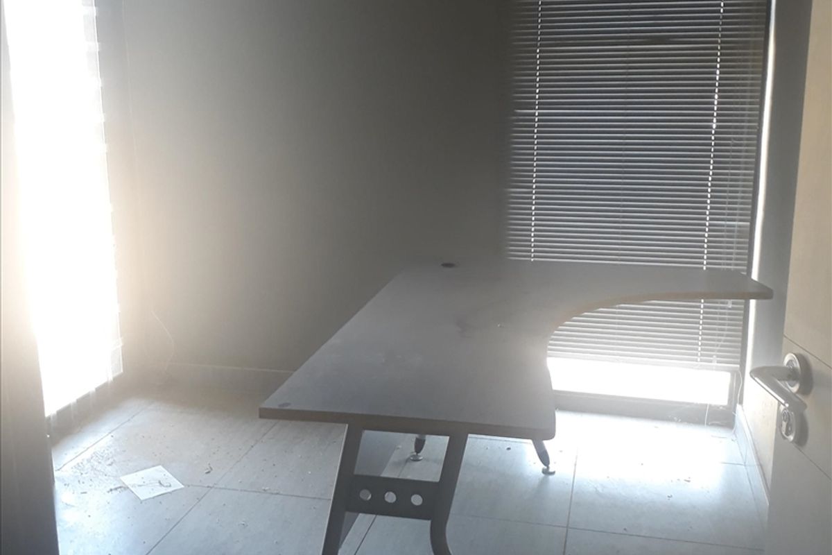 A functional office space featuring tiled flooring, venetian blinds, and natural light access through a glass sliding door.
