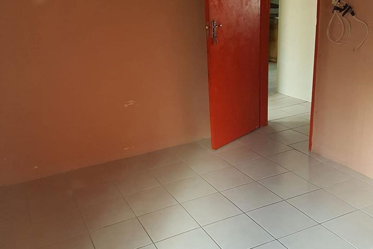 An empty bedroom featuring tiled flooring and a painted interior door, requiring minor cosmetic updates and electrical finishing.