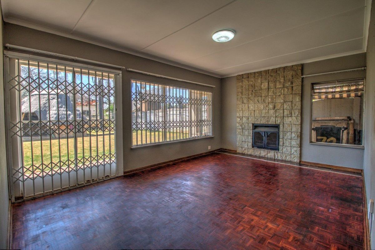 Spacious living room featuring a stone fireplace, parquet flooring, and large windows with security gates, offering direct access to the garden.
