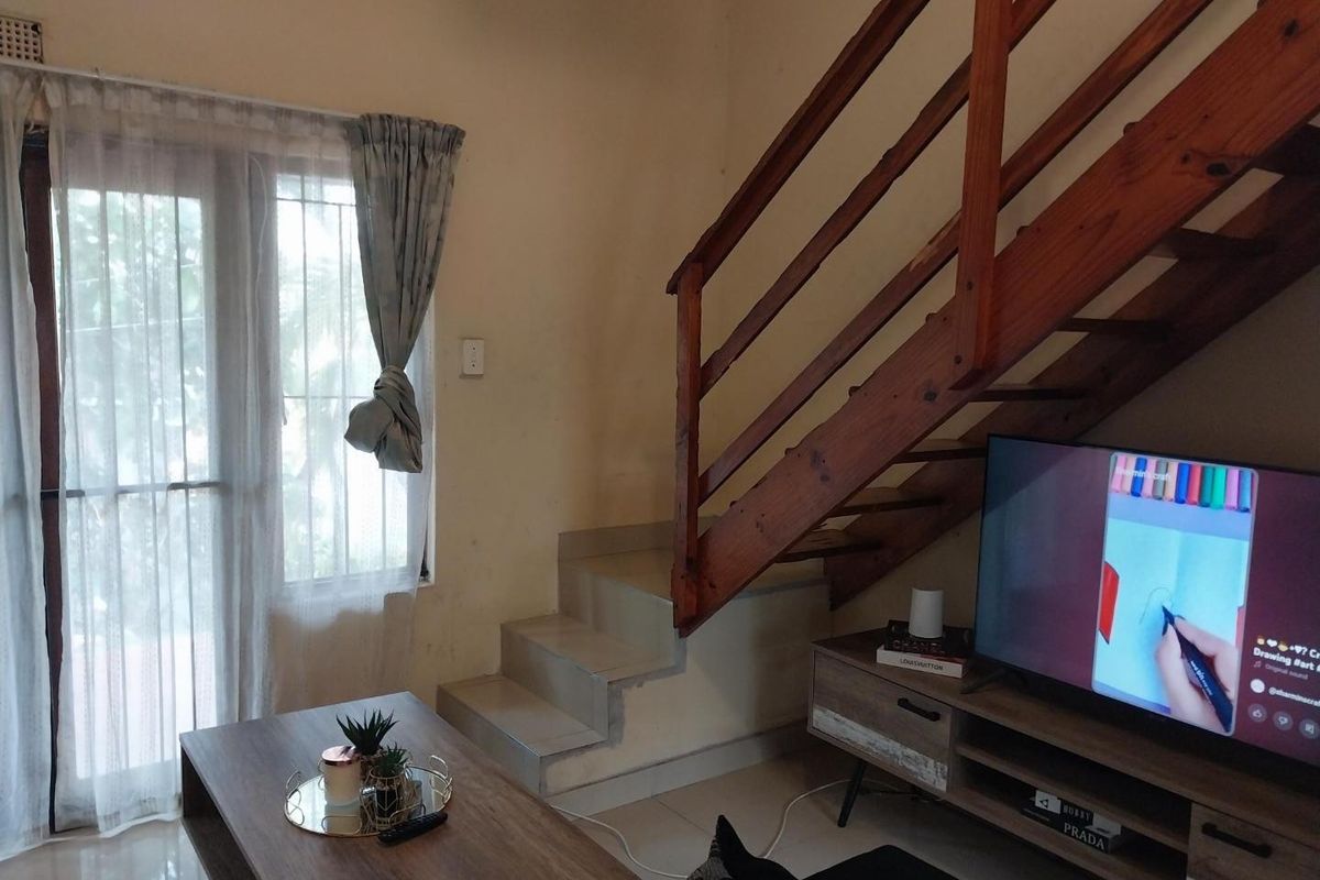 Living room area featuring a wooden staircase, tiled flooring, and a sliding door with security gate access to the exterior.