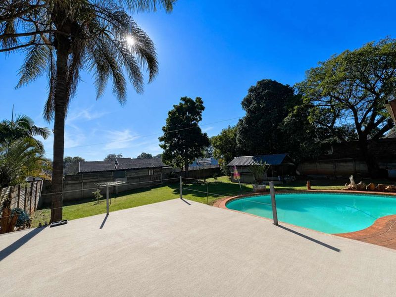 A spacious backyard featuring a swimming pool, a concrete patio area, and a well-maintained lawn surrounded by mature trees and perimeter fencing.