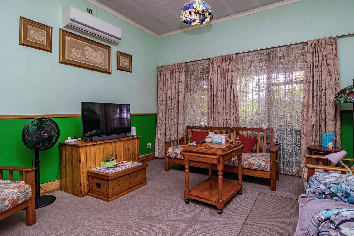 A living room featuring a wall-mounted air conditioning unit, large window with curtains, and carpeted flooring.
