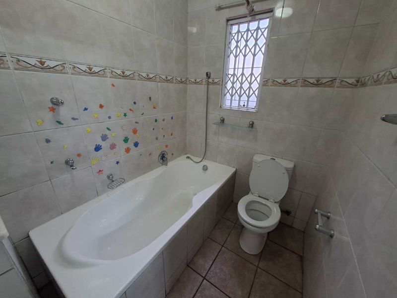 A functional bathroom featuring a built-in bathtub, toilet, and neutral ceramic tiling throughout, offering a clean and practical space.