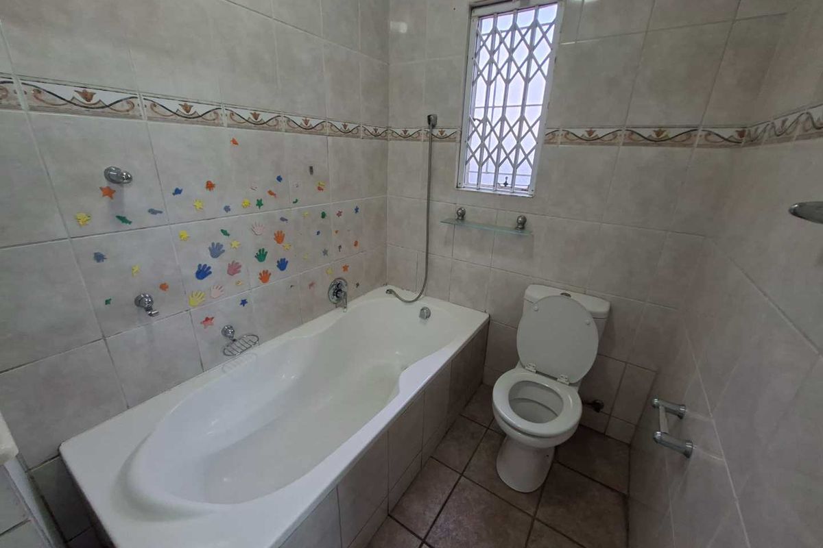 A functional bathroom featuring a built-in bathtub, toilet, and neutral ceramic tiling throughout, offering a clean and practical space.