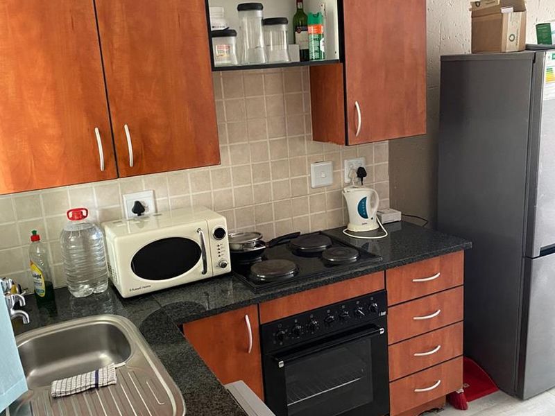 Compact kitchen featuring laminate cabinetry, granite countertops, tiled backsplash, and built-in oven with electric hob.