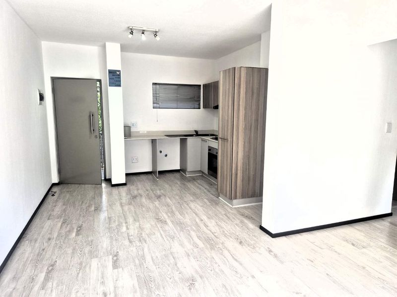 An open-plan living and kitchen area featuring light wood-look laminate flooring, modern cabinetry, built-in appliances, and neutral finishes throughout.