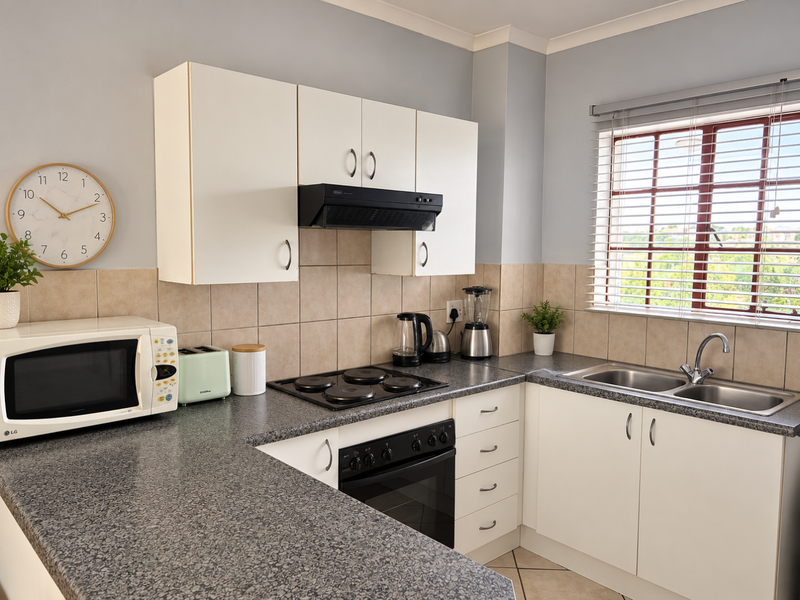 A functional kitchen featuring laminate countertops, built-in cabinetry, an electric hob with extractor fan, and a double bowl stainless steel sink.