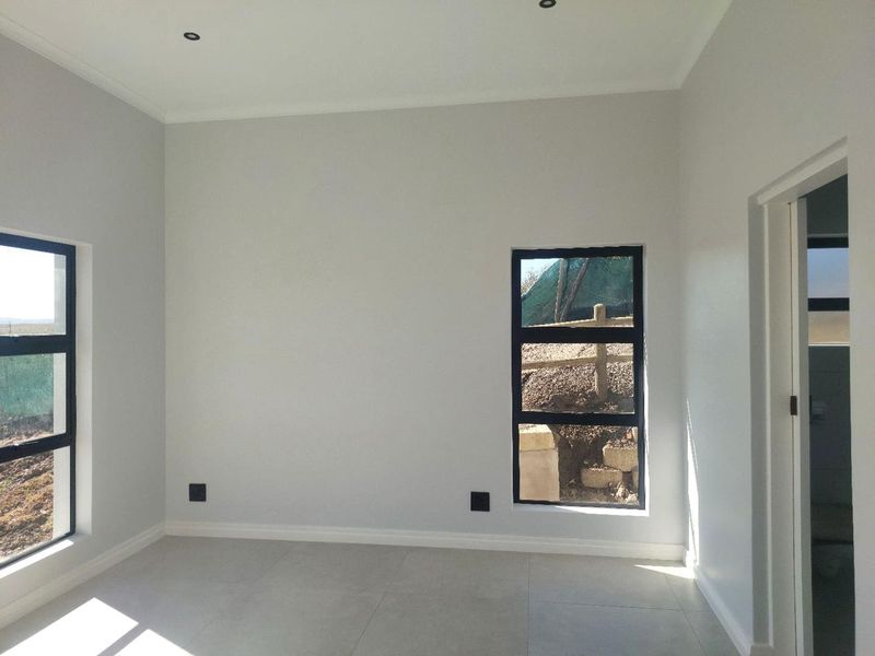 A bright, modern, and empty bedroom featuring neutral tiled flooring, recessed downlights, and black aluminium window frames.