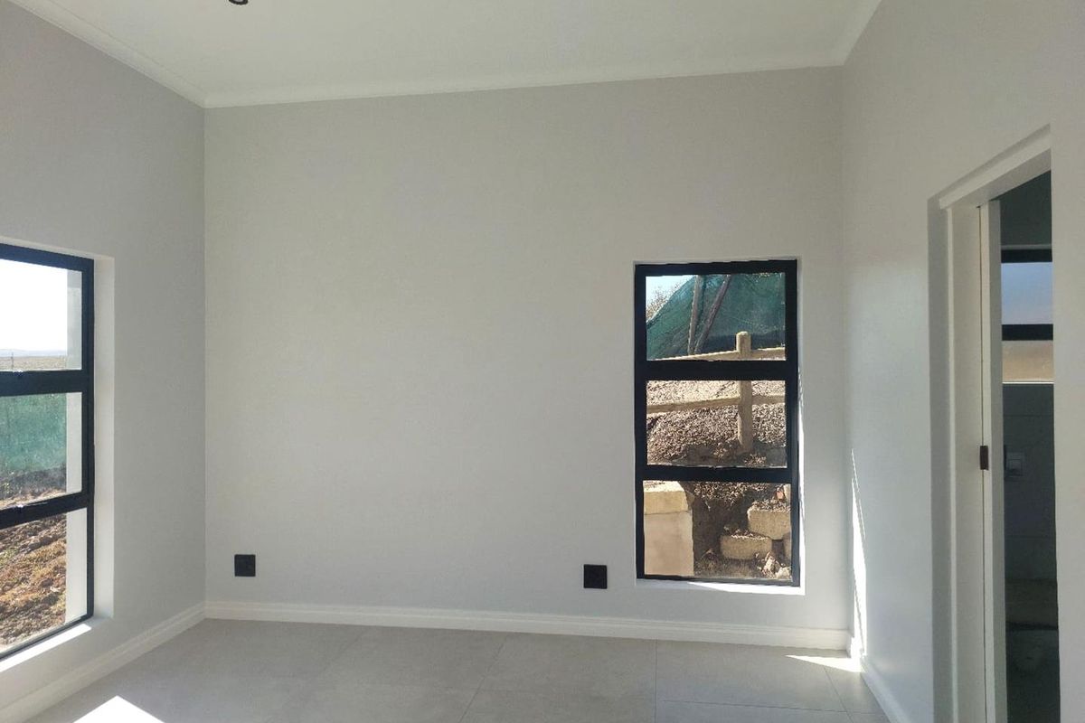 A bright, modern, and empty bedroom featuring neutral tiled flooring, recessed downlights, and black aluminium window frames.