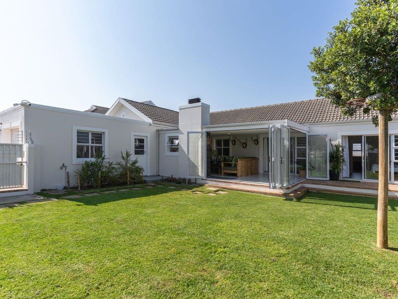 Rear view of the property featuring a well-maintained lawn, paved patio area, and bi-fold doors leading into the home with an integrated outdoor fireplace.