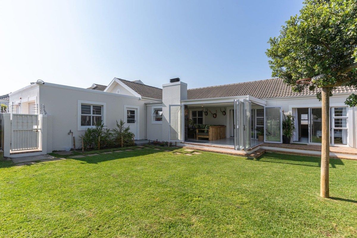 Rear view of the property featuring a well-maintained lawn, paved patio area, and bi-fold doors leading into the home with an integrated outdoor fireplace.