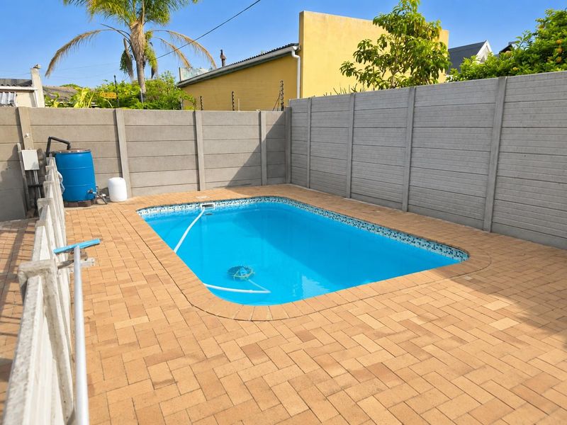 A private outdoor swimming pool area featuring a paved deck and secure precast concrete boundary walling.