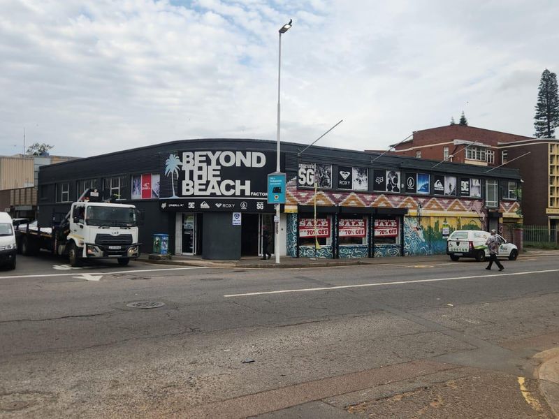 Street-level view of a commercial retail building featuring large display windows and prominent signage on a corner lot.
