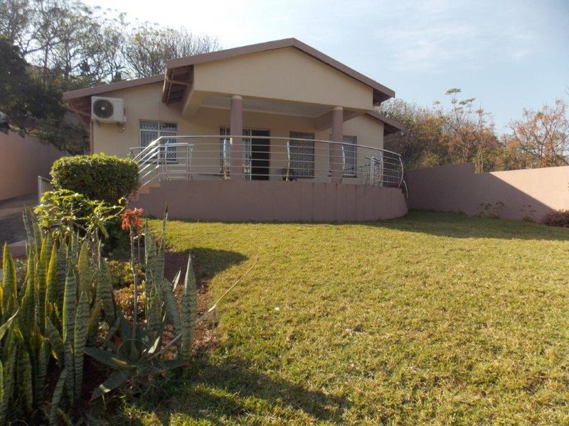 Rear view of the house featuring a covered patio with a stainless steel balustrade, set within a landscaped garden area.