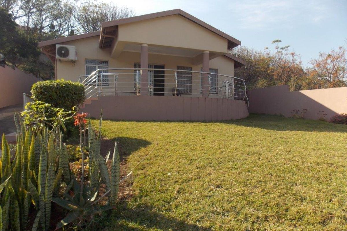 Rear view of the house featuring a covered patio with a stainless steel balustrade, set within a landscaped garden area.