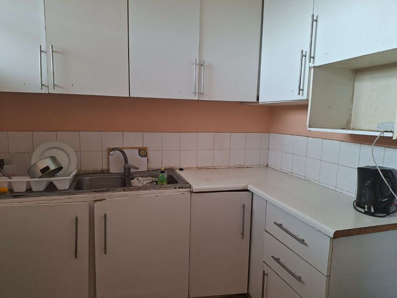 A compact kitchen featuring white cabinetry, laminate countertops, and a stainless steel double sink with a tiled splashback.