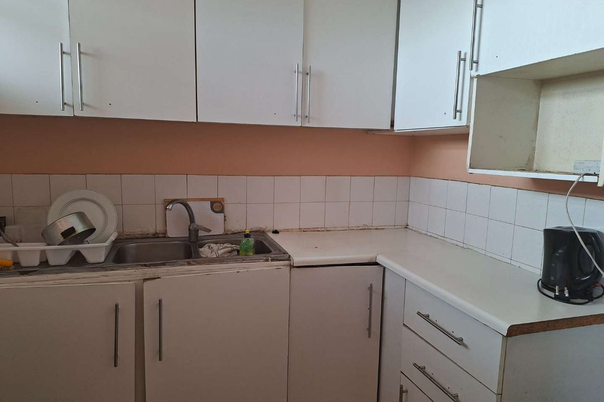 A compact kitchen featuring white cabinetry, laminate countertops, and a stainless steel double sink with a tiled splashback.
