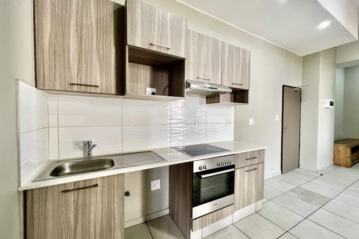 Modern kitchen featuring wood-grain cabinetry, integrated oven and hob, stainless steel sink, and tiled flooring in an open-plan layout.