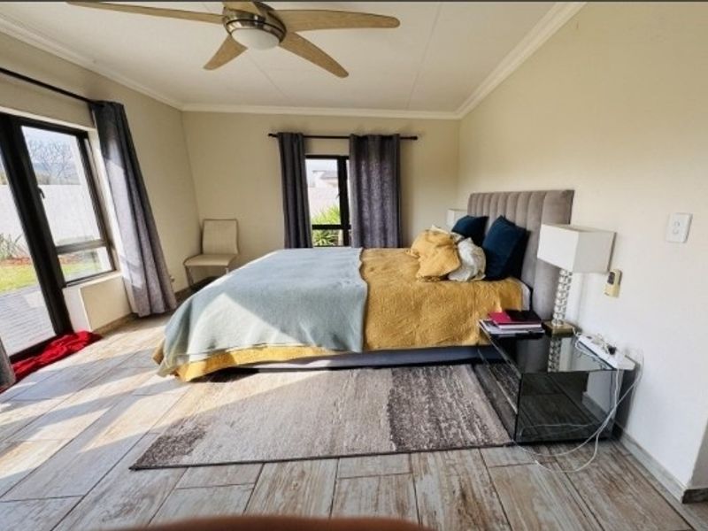 A well-lit bedroom featuring tiled flooring, a ceiling fan, and large sliding glass doors providing direct access to the outdoor area.