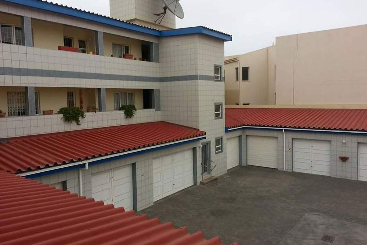 Exterior view of an apartment complex featuring a paved courtyard, multiple garage doors, and multi-level balconies with tiled facades and red roofing.