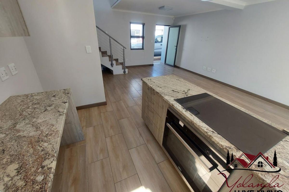 Open plan kitchen and living area featuring a central island with granite countertops, built-in oven, electric hob, and modern tiled flooring.