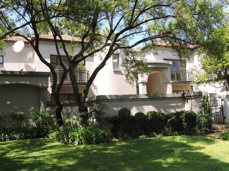 A well-maintained two-story residence featuring a terracotta tiled roof, arched entrance, and private balconies with wrought iron railings, set behind a landscaped garden.