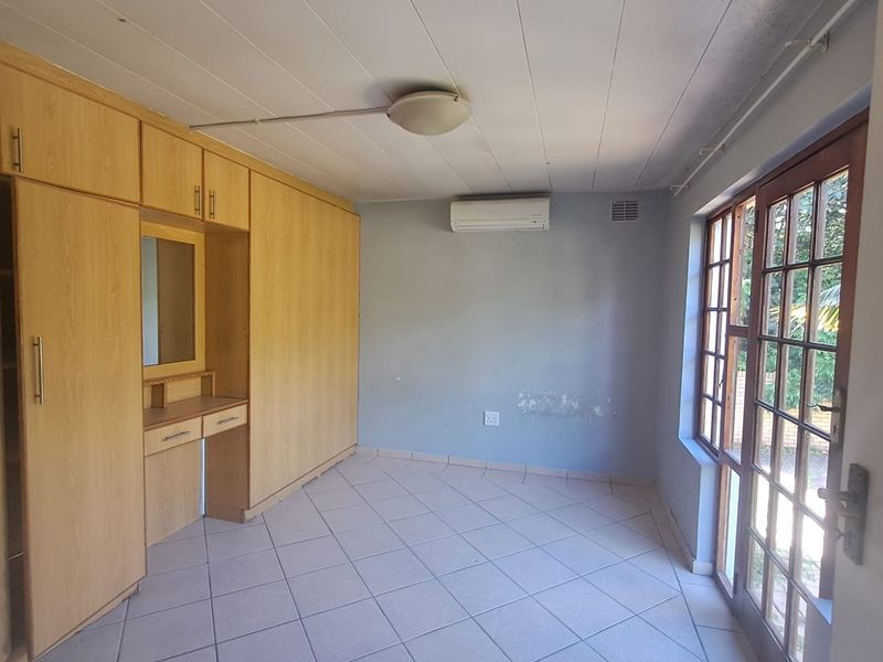 A bedroom featuring built-in wooden cupboards, tiled flooring, an air conditioning unit, and glass-paned french doors leading to the exterior.