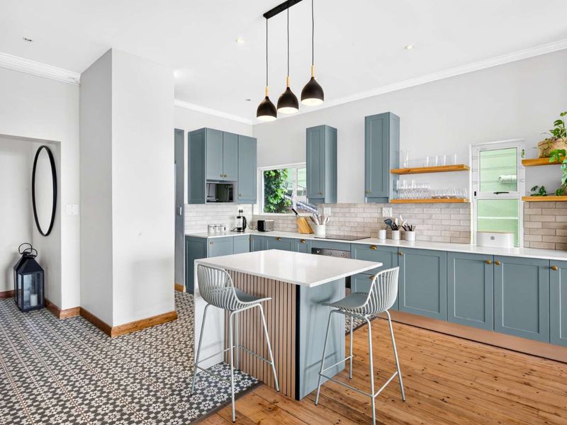 Modern kitchen featuring blue cabinetry, stone-topped island, subway tile backsplash, and a blend of timber and patterned tile flooring with stylish pendant lighting.
