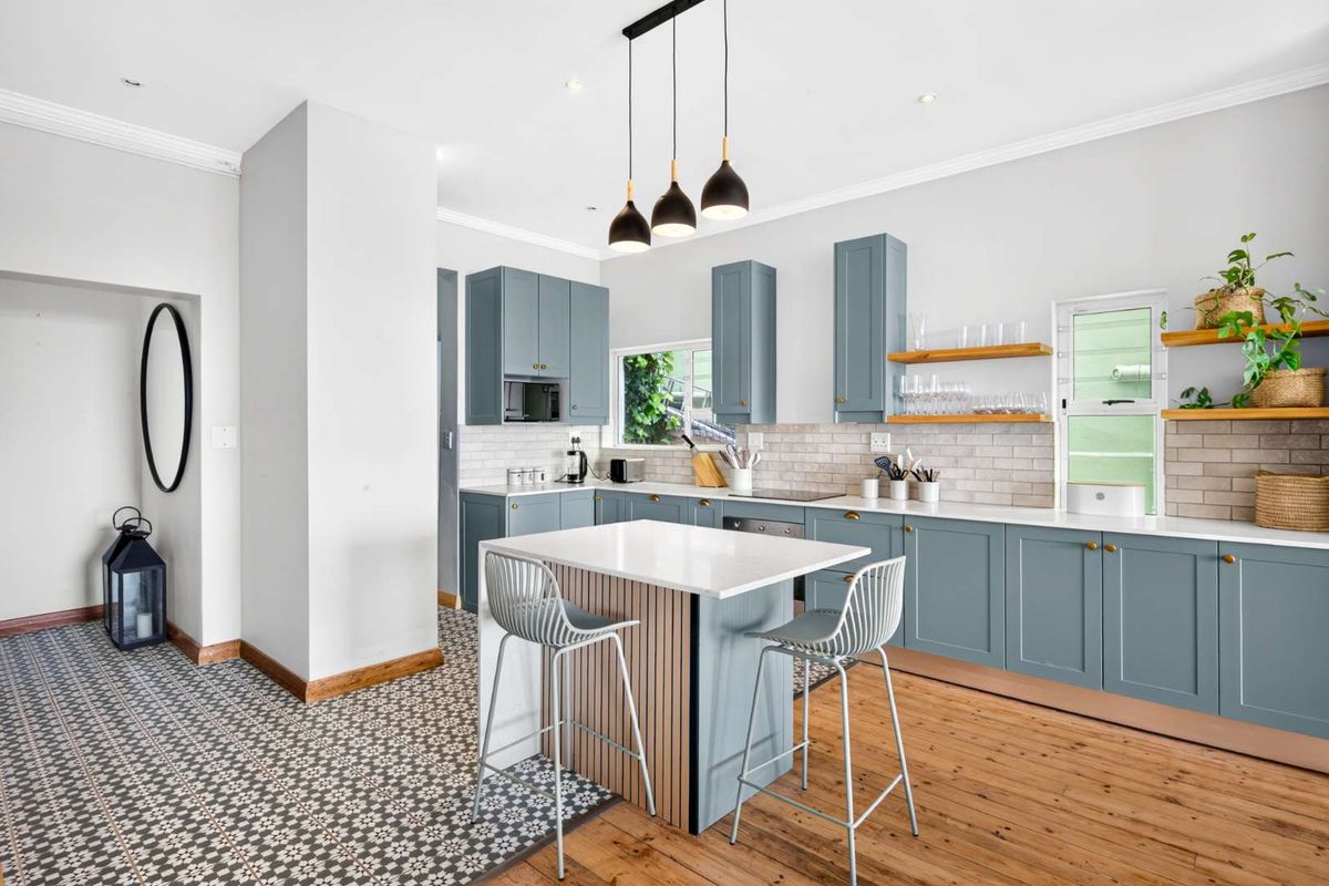 Modern kitchen featuring blue cabinetry, stone-topped island, subway tile backsplash, and a blend of timber and patterned tile flooring with stylish pendant lighting.