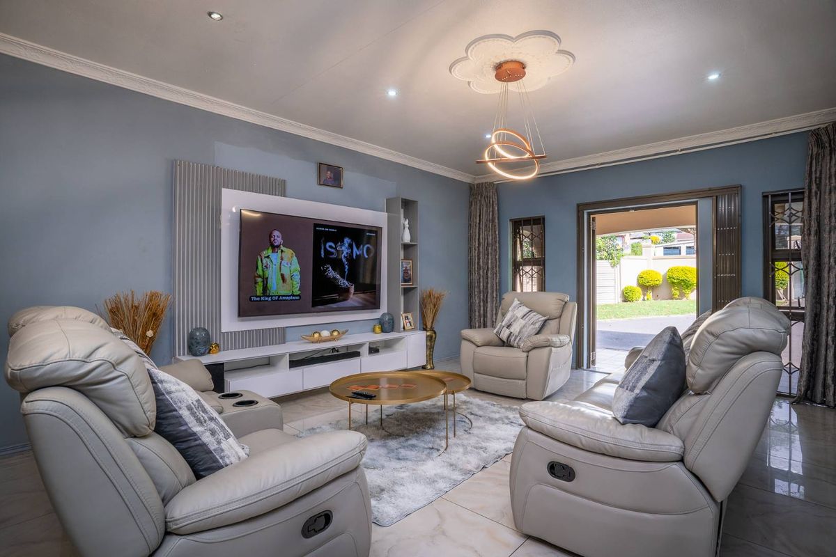 A well-maintained living room featuring a modern built-in media wall, tiled flooring, decorative ceiling rose, and direct access to the outdoor patio area.