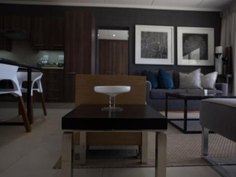 An open-plan living and kitchen area featuring dark wood cabinetry and neutral tiled flooring in a modern apartment setting.