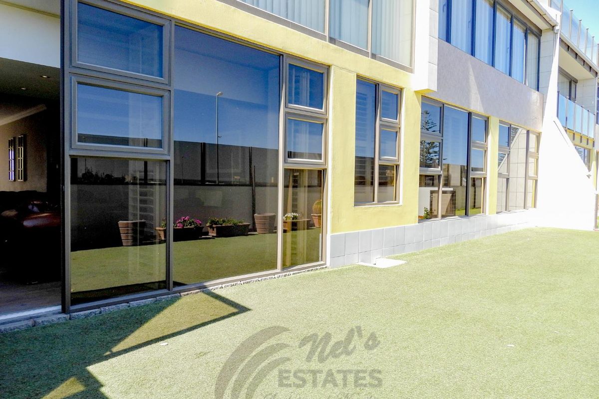 A view of the rear exterior of the apartment building, featuring large glass sliding doors, modern window frames, and a well-maintained artificial grass lawn.