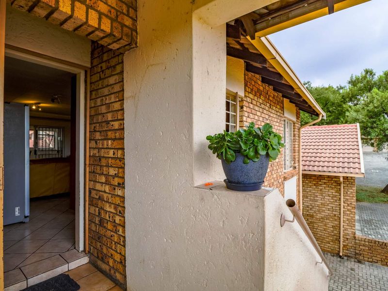 Covered balcony entrance featuring face brick detailing, tiled flooring, and a metal handrail, providing access to the interior living space.
