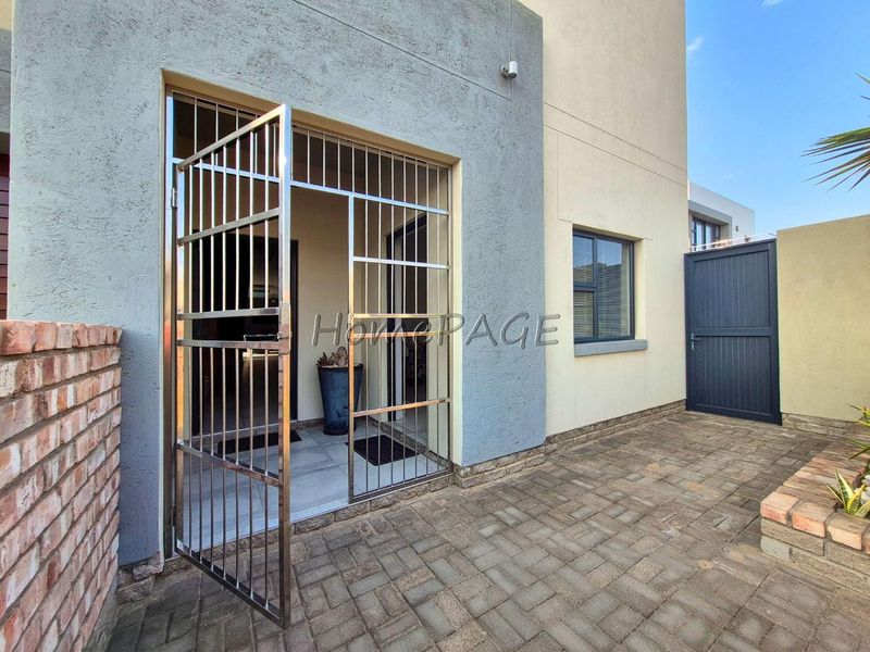 A well-maintained rear patio area featuring paved flooring, a secure stainless steel gate, and a brick boundary wall.