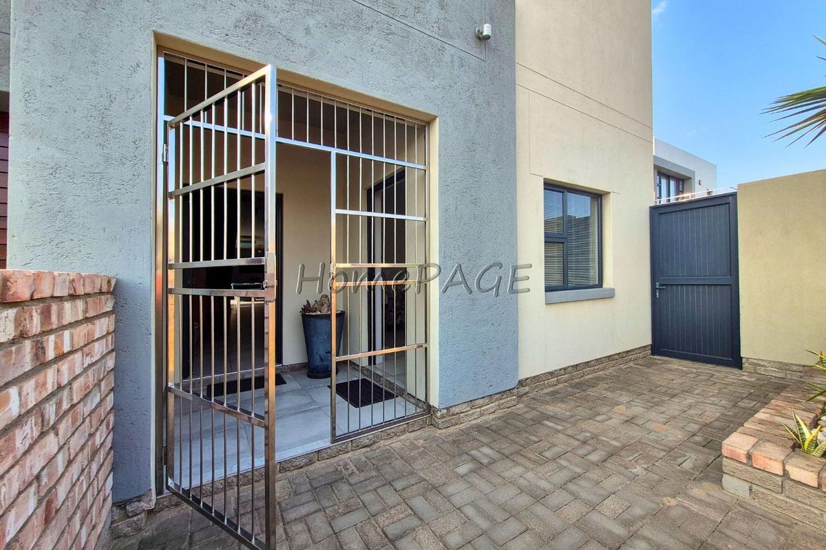 A well-maintained rear patio area featuring paved flooring, a secure stainless steel gate, and a brick boundary wall.