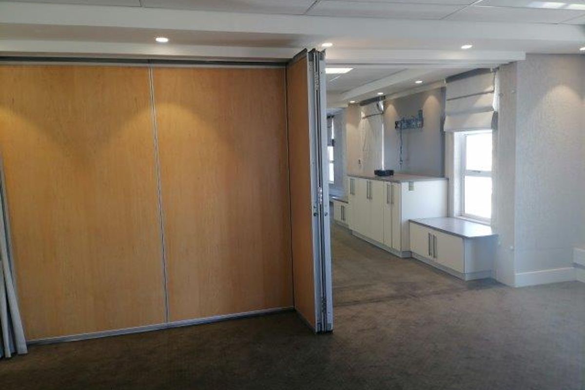 Spacious office area featuring a flexible operable partition wall, built-in storage cabinetry, and recessed ceiling lighting, offering a versatile professional workspace.