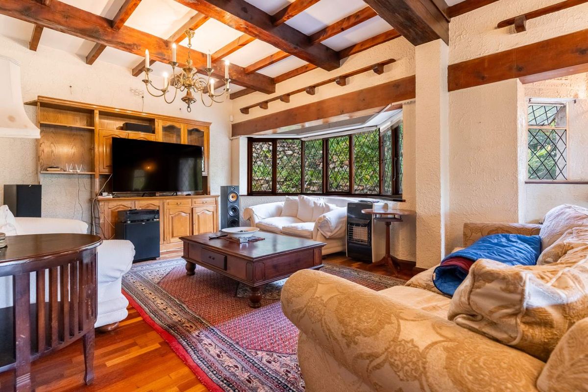 A cozy living room featuring exposed timber ceiling beams, leaded glass bay windows, and built-in wooden cabinetry, creating a traditional and warm atmosphere.