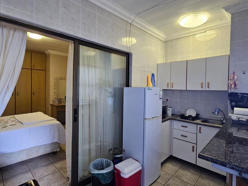 Open-plan apartment layout featuring a compact kitchen with granite countertops and tiled flooring, seamlessly connected to an adjacent bedroom with built-in storage.