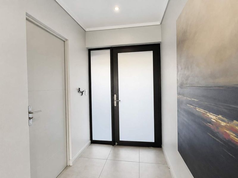 A clean and modern entrance hall featuring neutral tiled flooring, a contemporary frosted glass front door, and crisp, well-maintained wall finishes.