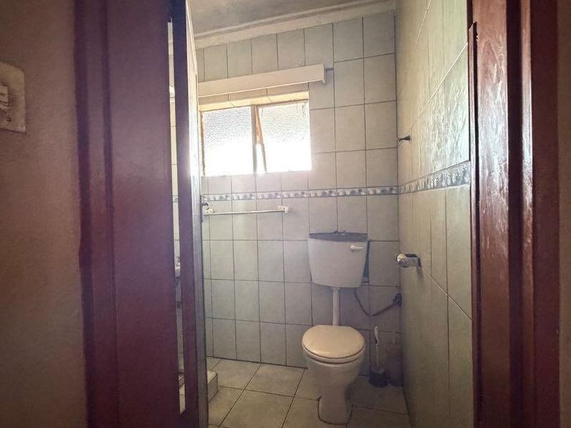 A compact bathroom featuring tiled walls and flooring, equipped with a standard toilet and window, currently in need of cosmetic updates.