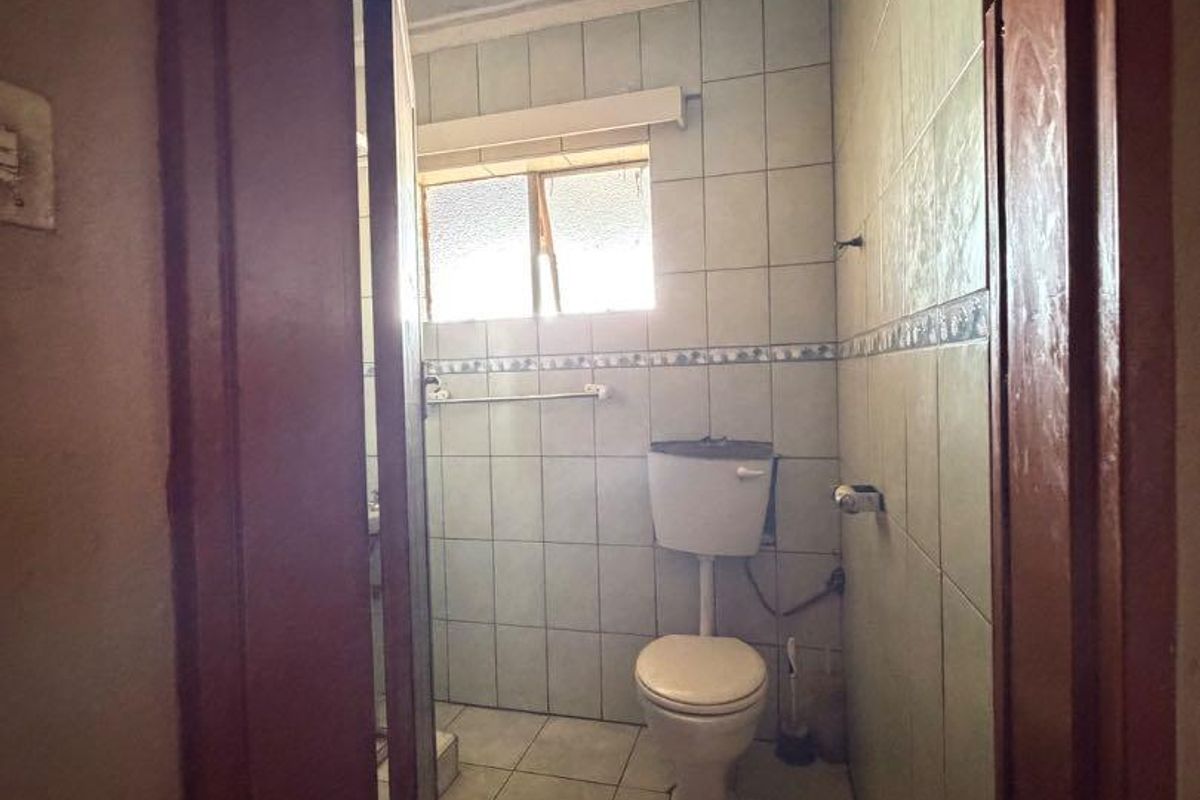 A compact bathroom featuring tiled walls and flooring, equipped with a standard toilet and window, currently in need of cosmetic updates.